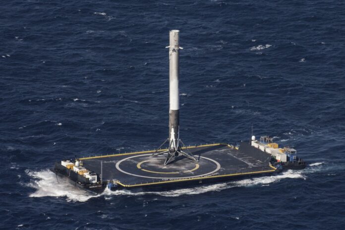 A SpaceX Falcon 9 first-stage booster standing upright on an autonomous drone ship in the Atlantic after landing