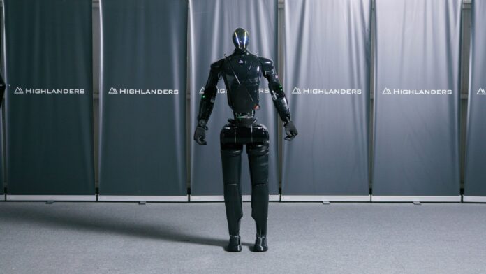 Highlanders' black humanoid robot N standing in front of branded backdrop panels