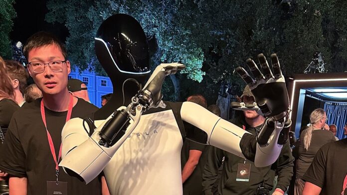 Tesla Optimus humanoid robot (16:9 crop) Tesla Optimus humanoid robot waving among a crowd at a Tesla event
