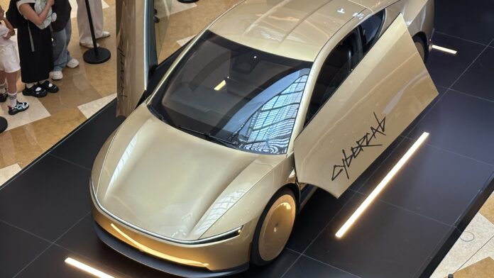A gold Tesla Cybercab two-seat robotaxi on display with its doors open