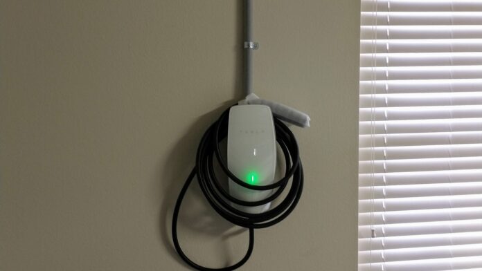 Tesla Wall Connector home charger mounted on a wall with its cable coiled and green status light on