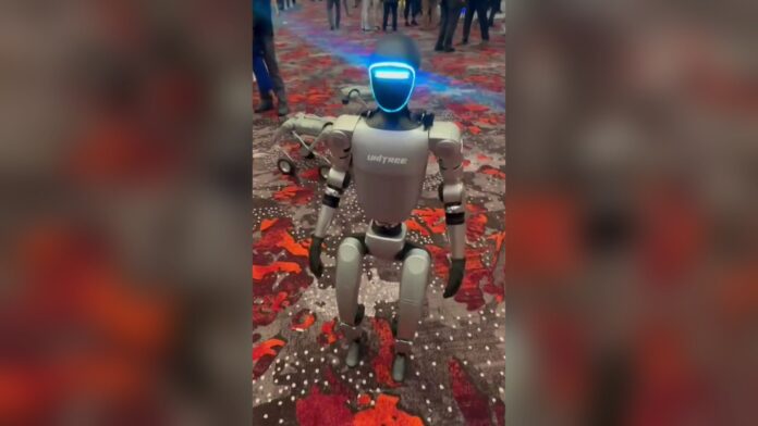 A Unitree G1 humanoid robot with a glowing blue face visor standing on a red patterned carpet at an expo