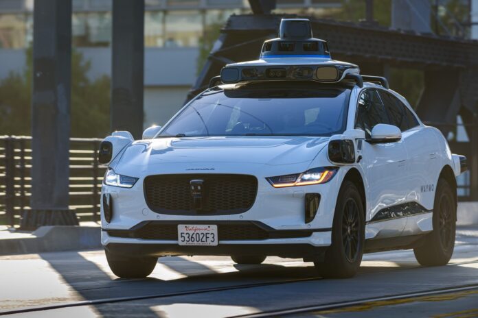 A white Waymo Jaguar I-Pace robotaxi with roof sensors crossing the 4th Street Bridge in San Francisco